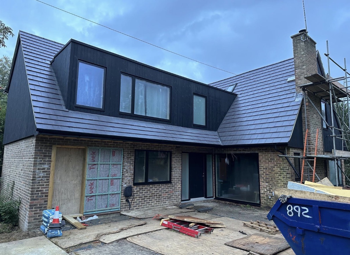 Grey tiled pitched roof around a black-clad dormer, with brick chimney and scaffolding still in place
